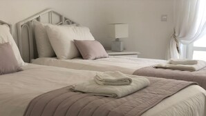 Et hotelværelse med to senge, hver med sengegavl, puder og et foldet håndklæde på sengen. Et natbord med en lampe er placeret imellem sengene.