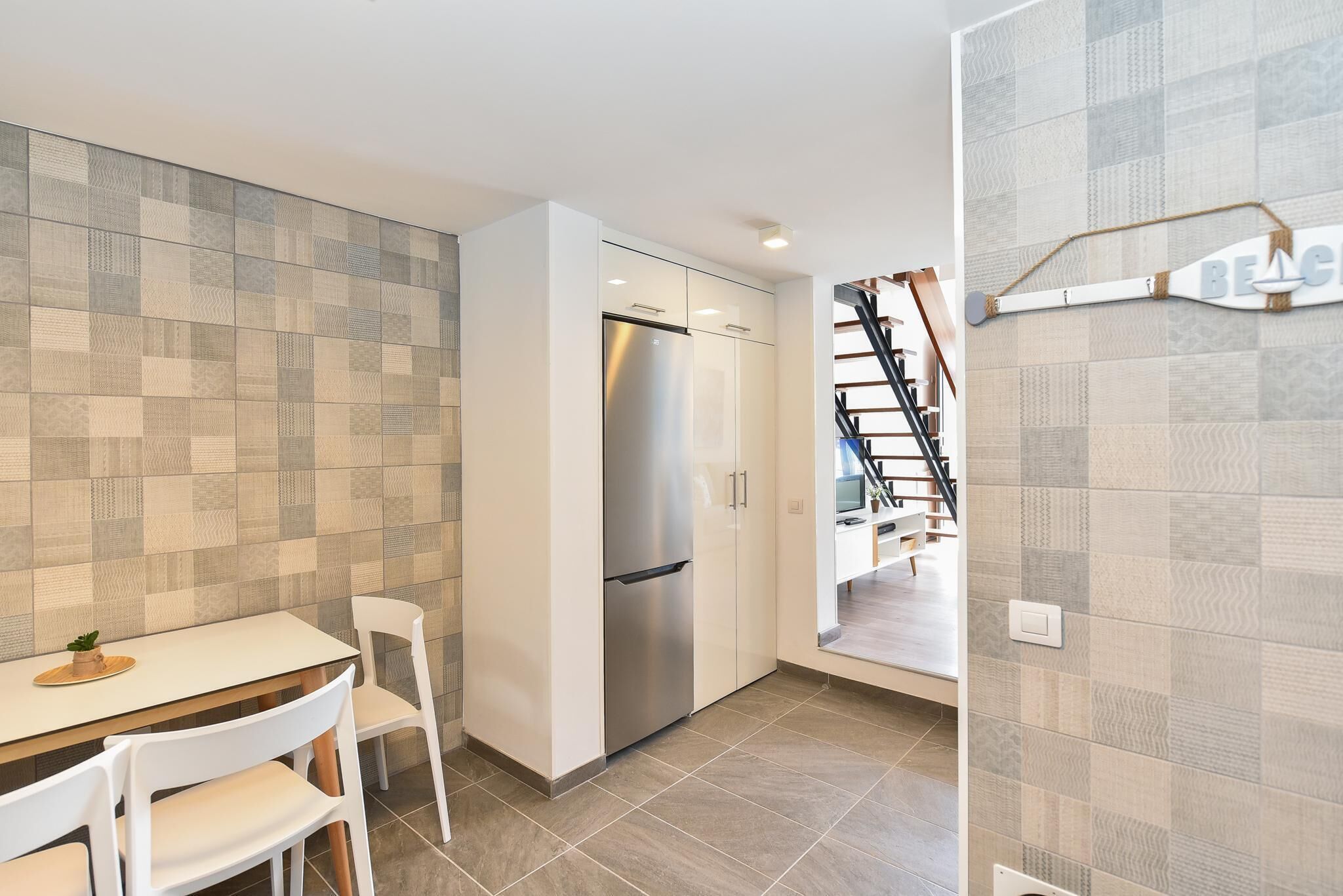A modern kitchen with a stainless steel refrigerator, white cabinetry, and a tiled backsplash.
