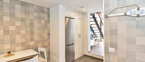 A modern kitchen with a stainless steel refrigerator, white cabinetry, and a tiled backsplash.