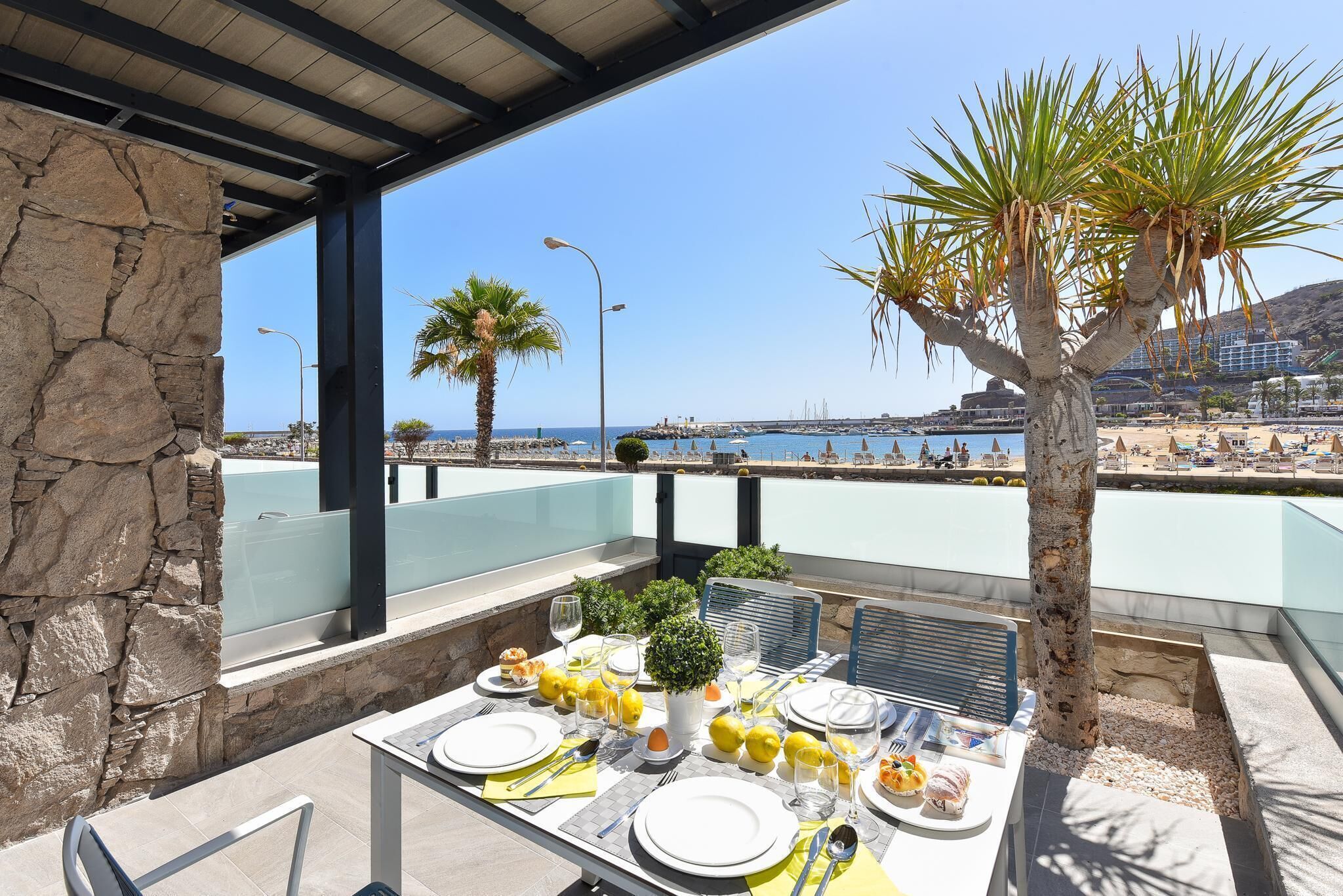 Un área de comedor al aire libre con una mesa dispuesta para dos personas, con vista a una playa y el mar.