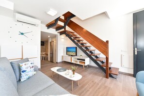 A modern living room with a wooden staircase, a white sofa, a coffee table, and a TV on a white cabinet.