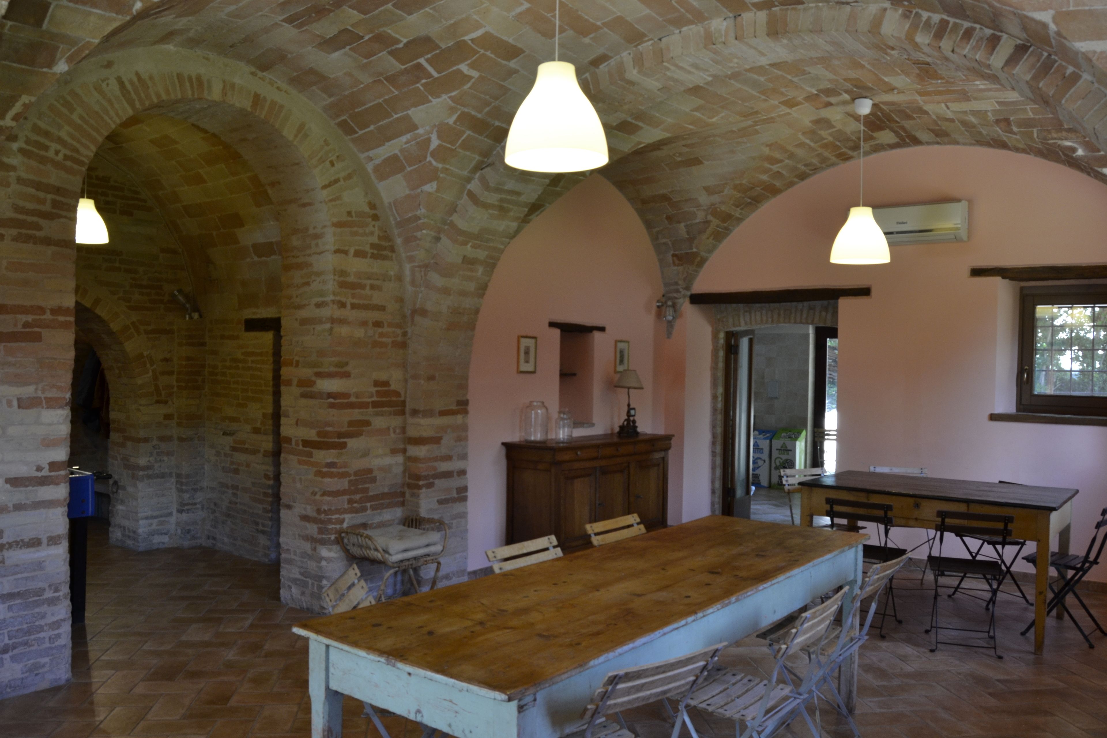 A room with a wooden table and chairs, brick arches, and hanging pendant lights.