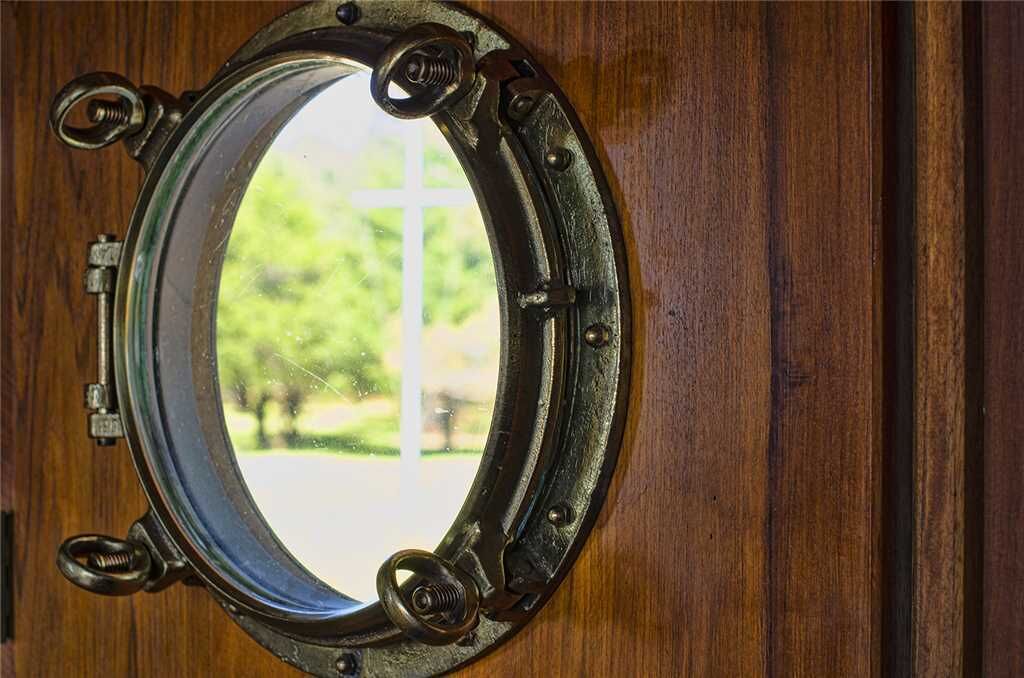A round window with a metal frame and four hinges, attached to a wooden door.