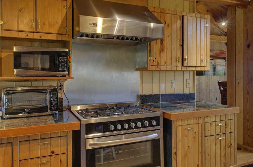 Une cuisine dotée de meubles en bois, d’une hotte en acier inoxydable, d’un four à micro-ondes et d’une cuisinière à gaz.