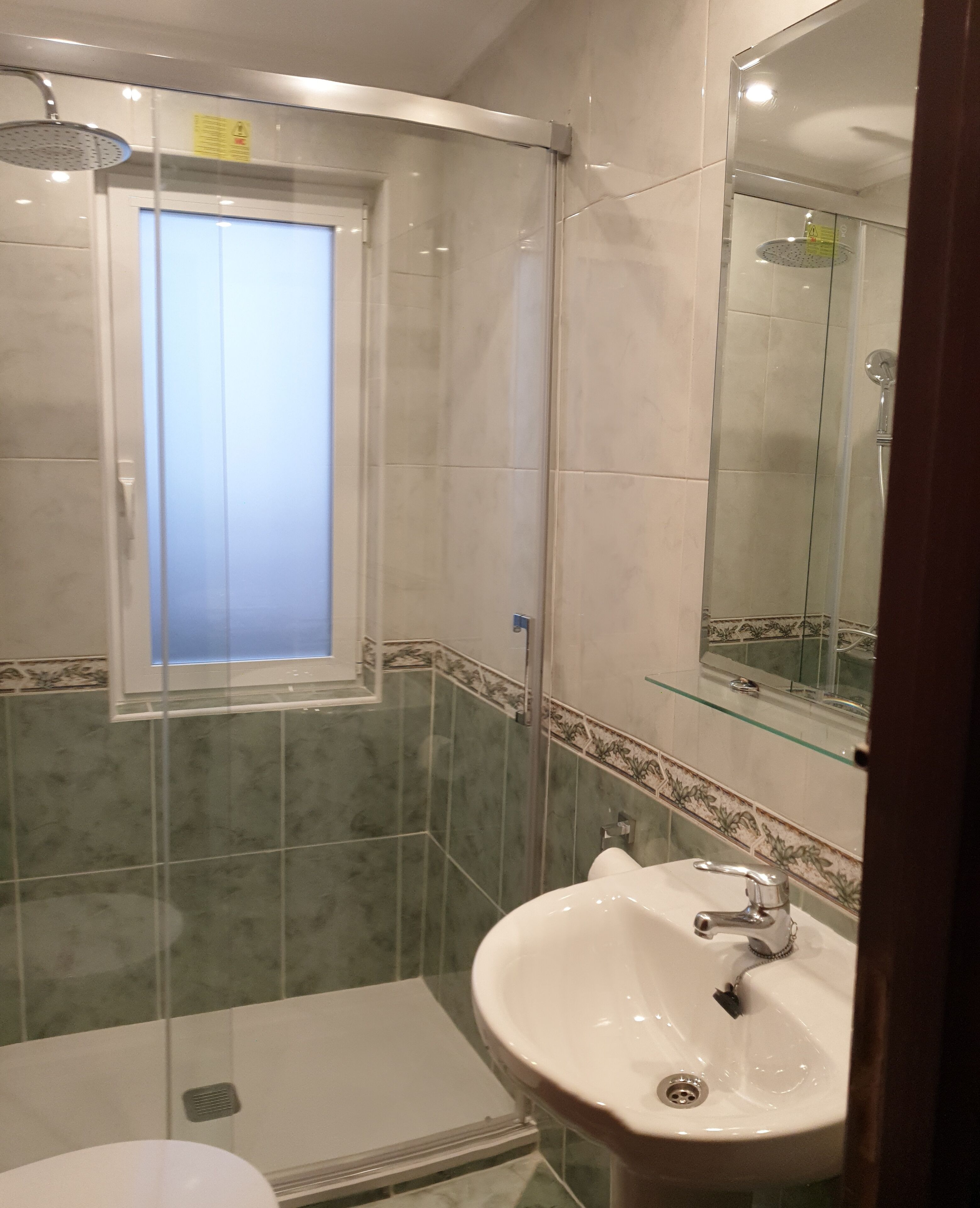 Un baño con cabina de ducha de vidrio, un lavabo con espejo y una ventana.