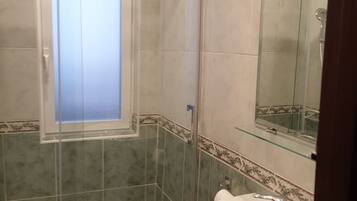 Un baño con cabina de ducha de vidrio, un lavabo con espejo y una ventana.