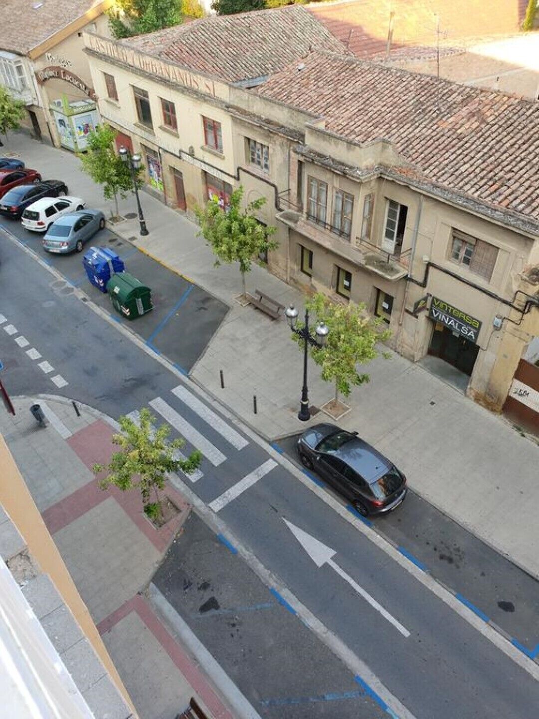 A street view with parked cars, a pedestrian crossing, and buildings with signage.
