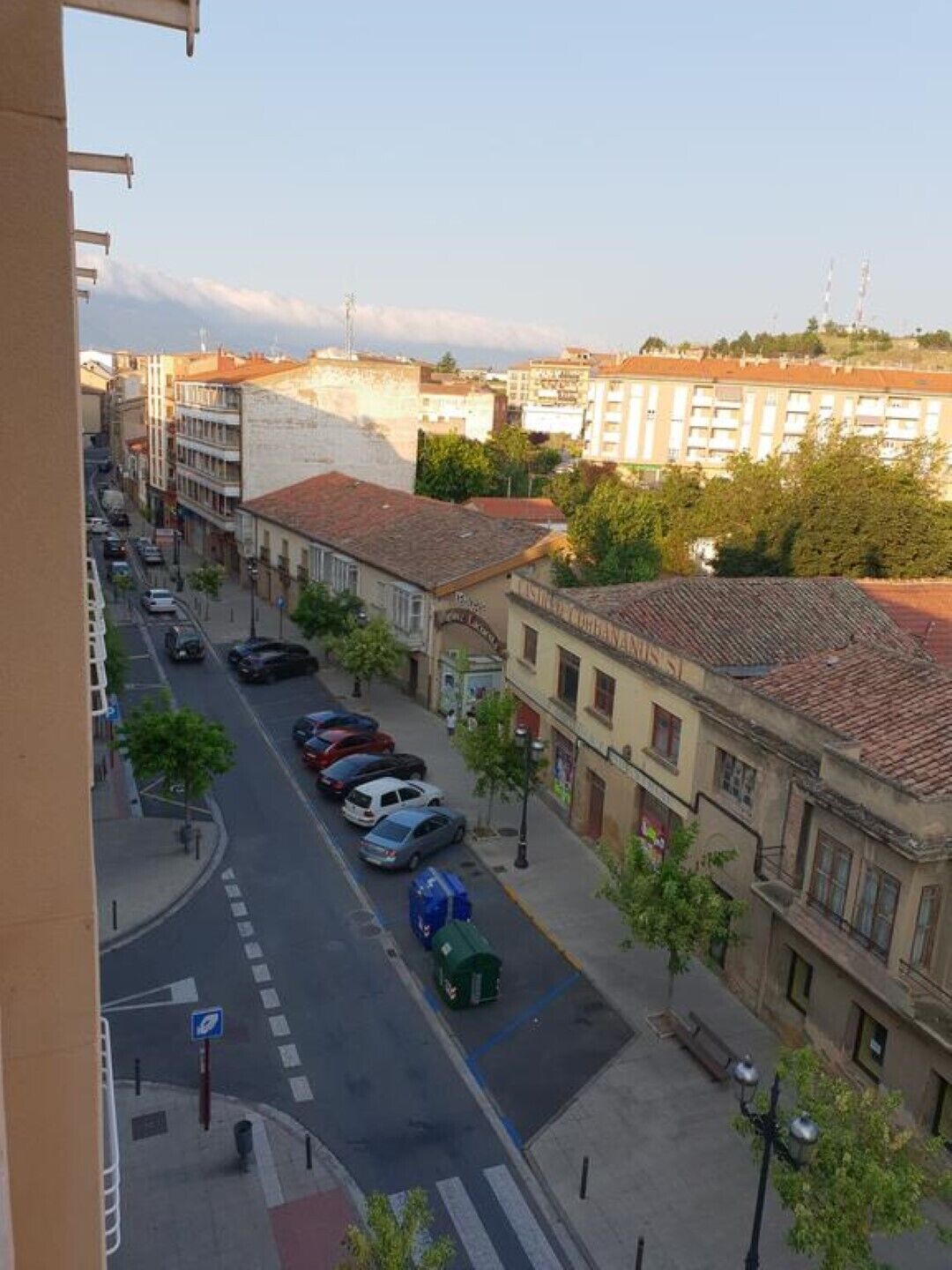 Vista de la calle con coches aparcados, edificios y cielo despejado.