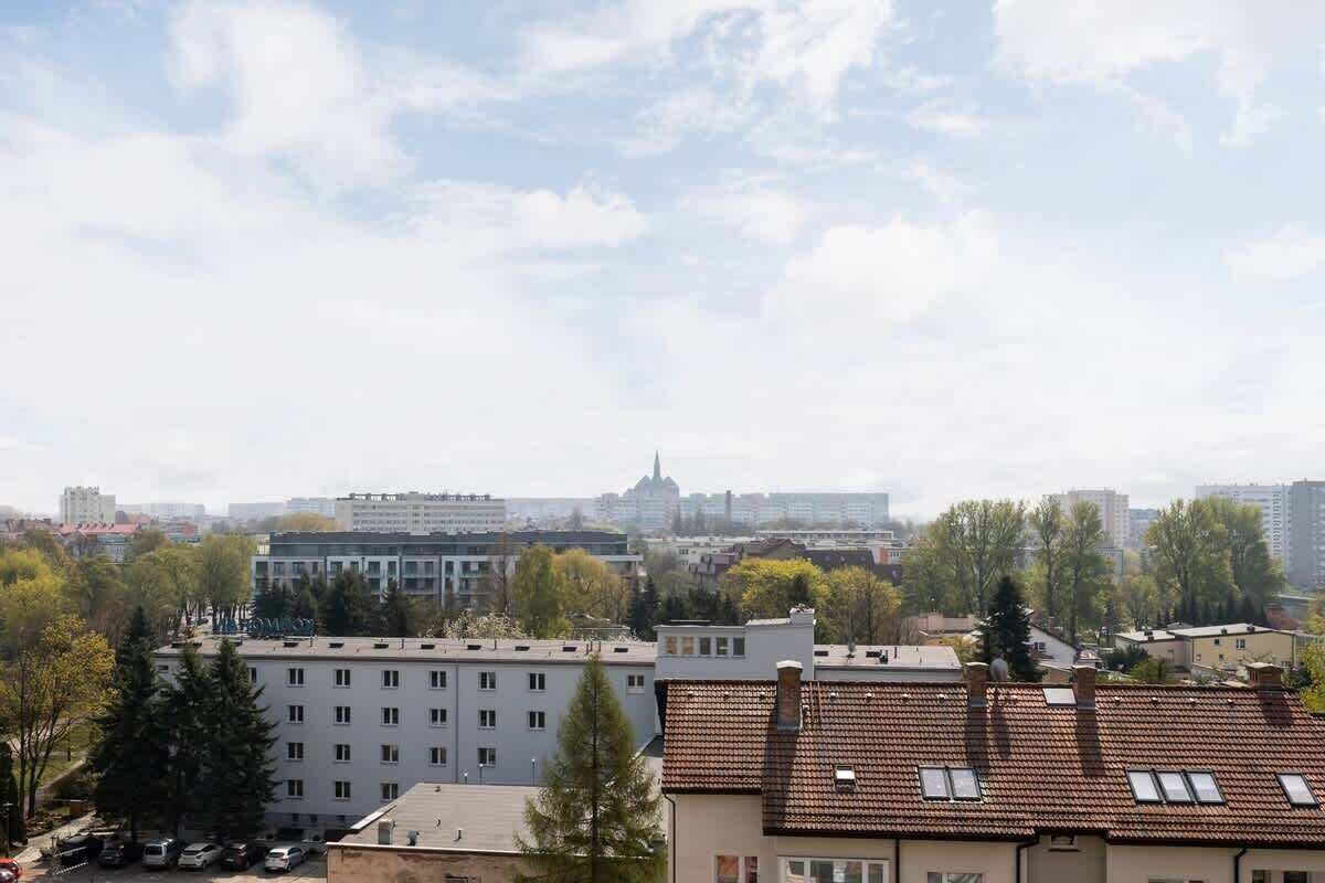 Ein Wohngebiet mit mehrstöckigen Gebäuden, einem markanten Kirchturm in der Ferne und einer Mischung aus Bäumen und parkenden Autos.