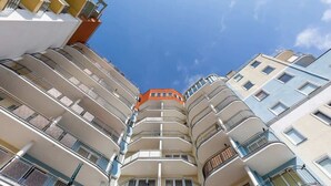 Un edificio residencial de varios pisos con balcones, cielo despejado y un edificio naranja prominente en la parte superior.