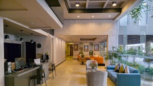 Una moderna hall d'albergo con reception, area lounge e ampie finestre che offrono vista all'esterno.