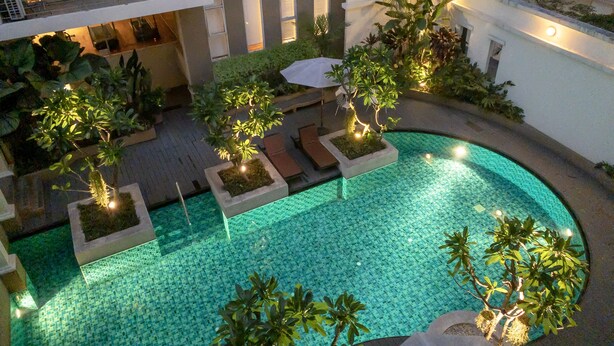 Una piscina sul tetto con pavimento piastrellato, circondata da fioriere con piccoli alberi e un'area relax con tavolo e sedie.