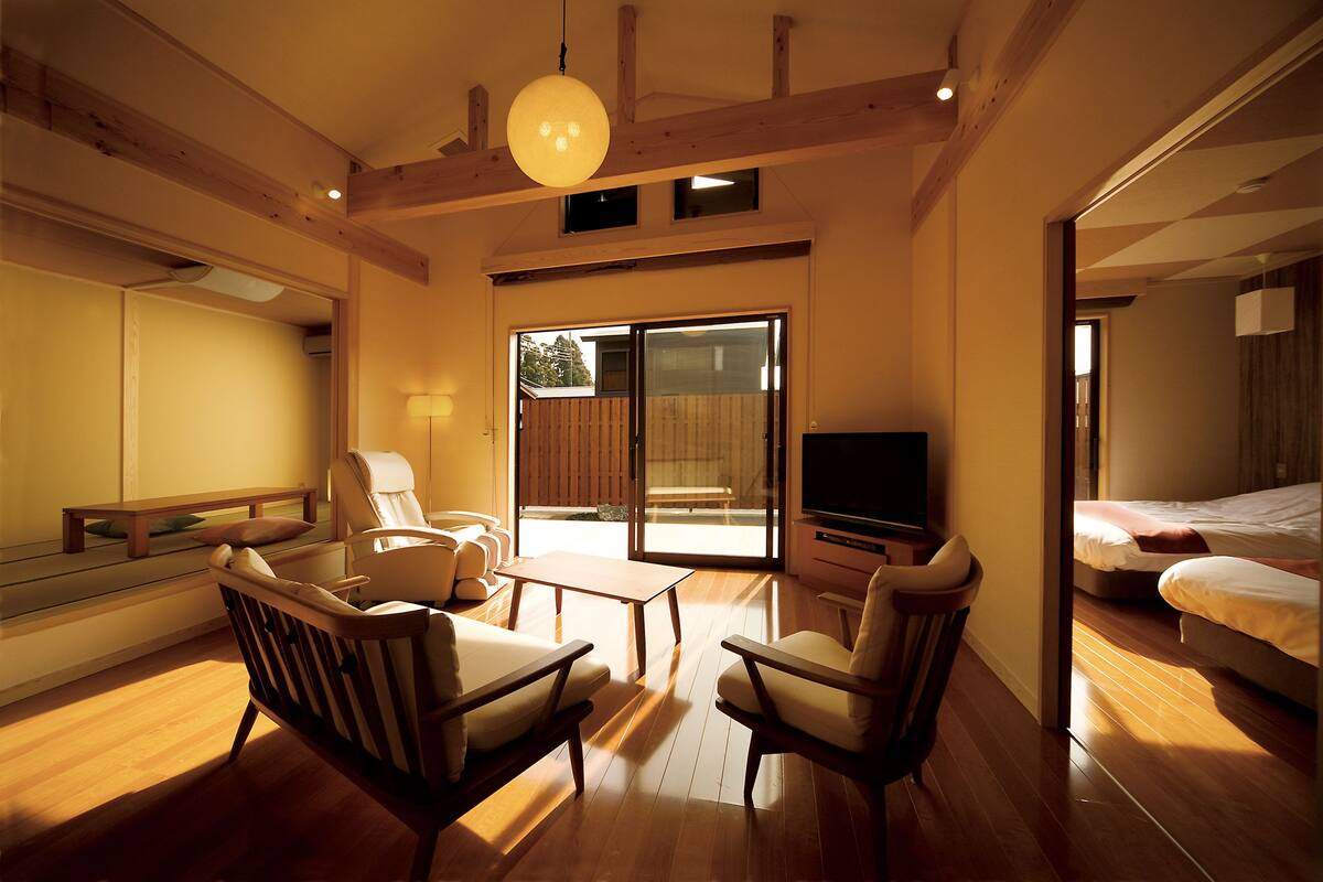A spacious living area with wooden flooring, a large sliding glass door leading to a balcony, and a television.