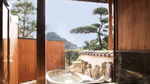 Un onsen japonés tradicional con interior de madera, una fuente termal de piedra y vistas a un paisaje montañoso.