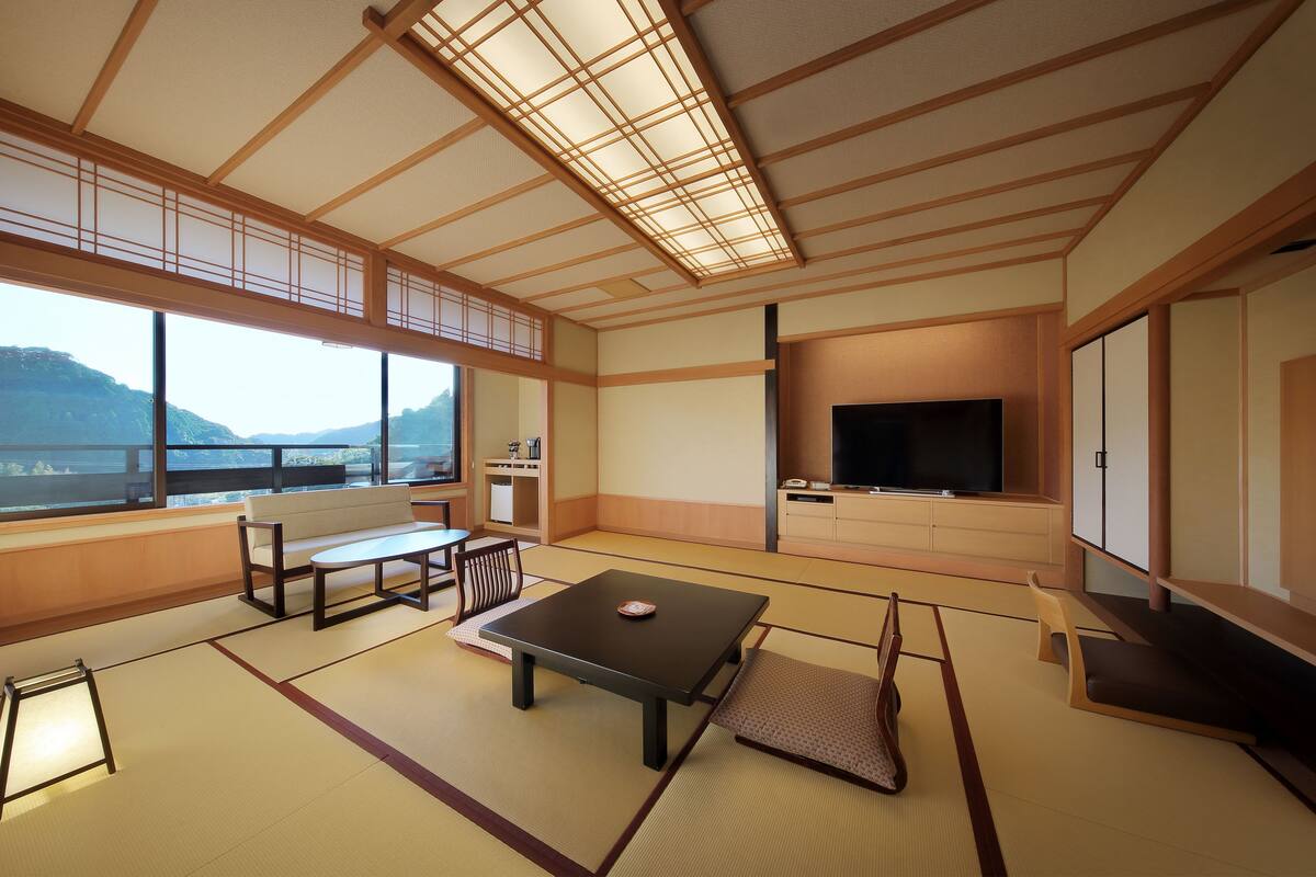 A traditional Japanese-style room with tatami flooring, a low table, a sofa, and a television.