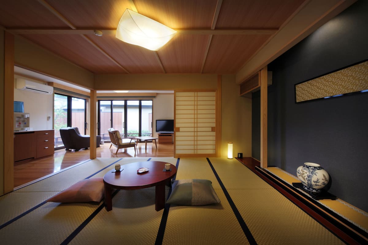A traditional Japanese room with tatami flooring, a low table, cushions, a television, and sliding doors leading to a balcony.