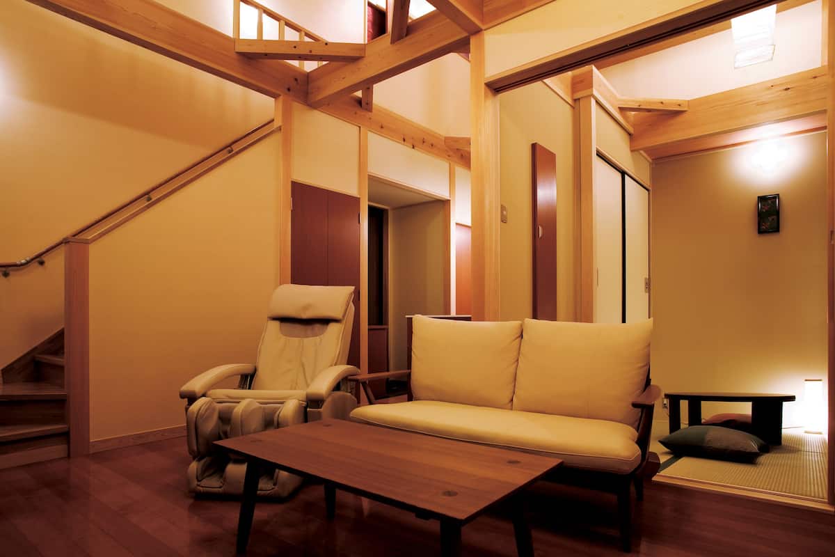 A room with a wooden staircase, a sofa, a recliner, and a small table.
