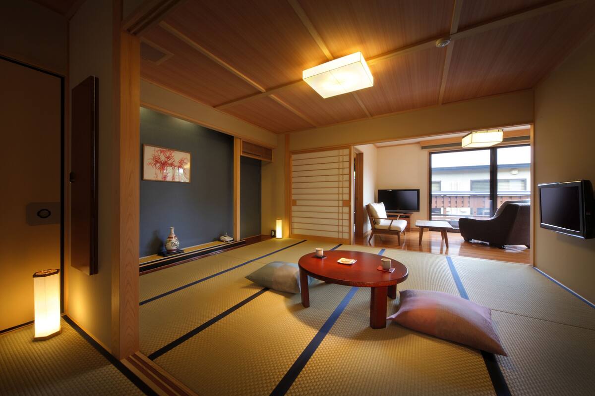 A traditional Japanese room with tatami flooring, a low wooden table, a television, and a sliding door leading to another room.