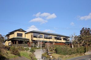 A two-story residential building with a green roof, multiple windows, and a well-maintained garden with various plants and a small pond. - Ryokusuitei (Kamogawa)