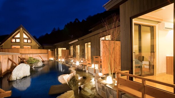 Un área de spa con aguas termales, una terraza de madera y un edificio con grandes ventanales.