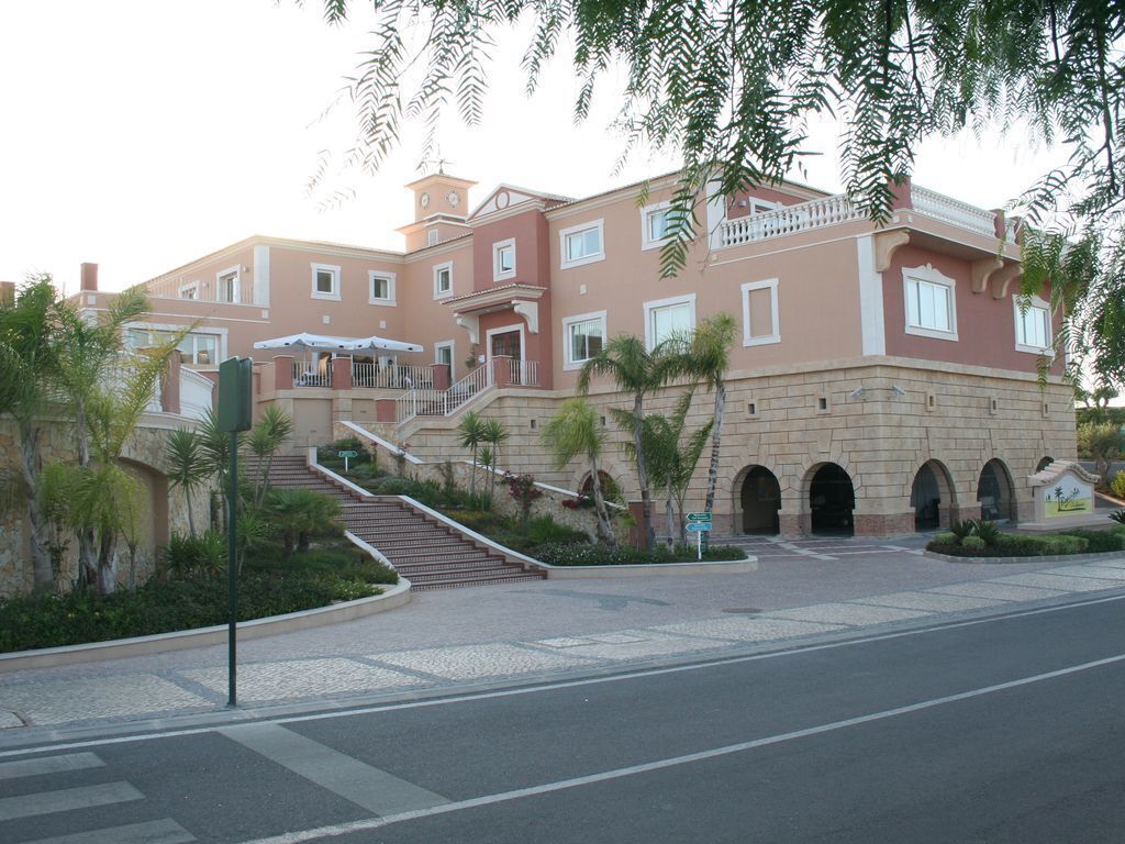 Un edificio de varios pisos con una escalera central, un balcón y un acceso empedrado.