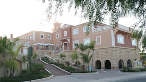 Un edificio de varios pisos con una escalera central, un balcón y un acceso empedrado.