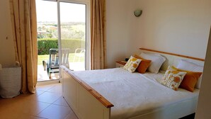 Un dormitorio con cama, cortinas, vista al exterior y piso de baldosas.