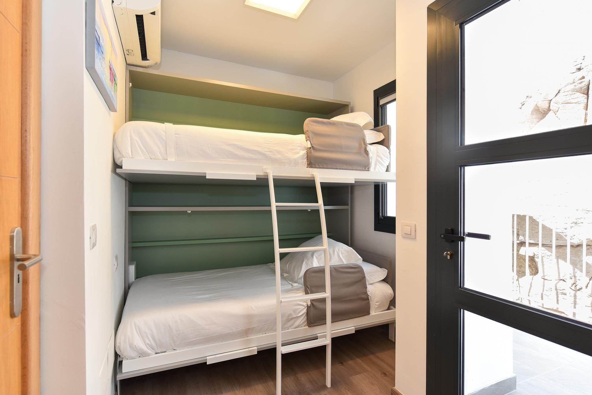 Une chambre avec un lit superposé, une échelle, une fenêtre et une porte.