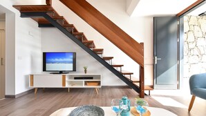 Ein modernes Wohnzimmer mit einer Holztreppe, einem Flachbildfernseher, einer weißen Unterhaltungsecke und einem Essbereich mit einem weißen Tisch und blauem Glasgeschirr.