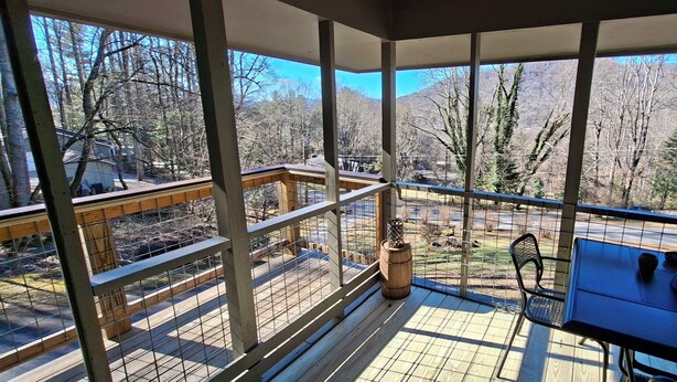 Un espacio al aire libre techado con una terraza de madera, una mesa con sillas y vistas a zona boscosa.