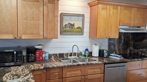 Una cocina con armarios de madera, microondas, cafetera y lavamanos con encimera de mármol.