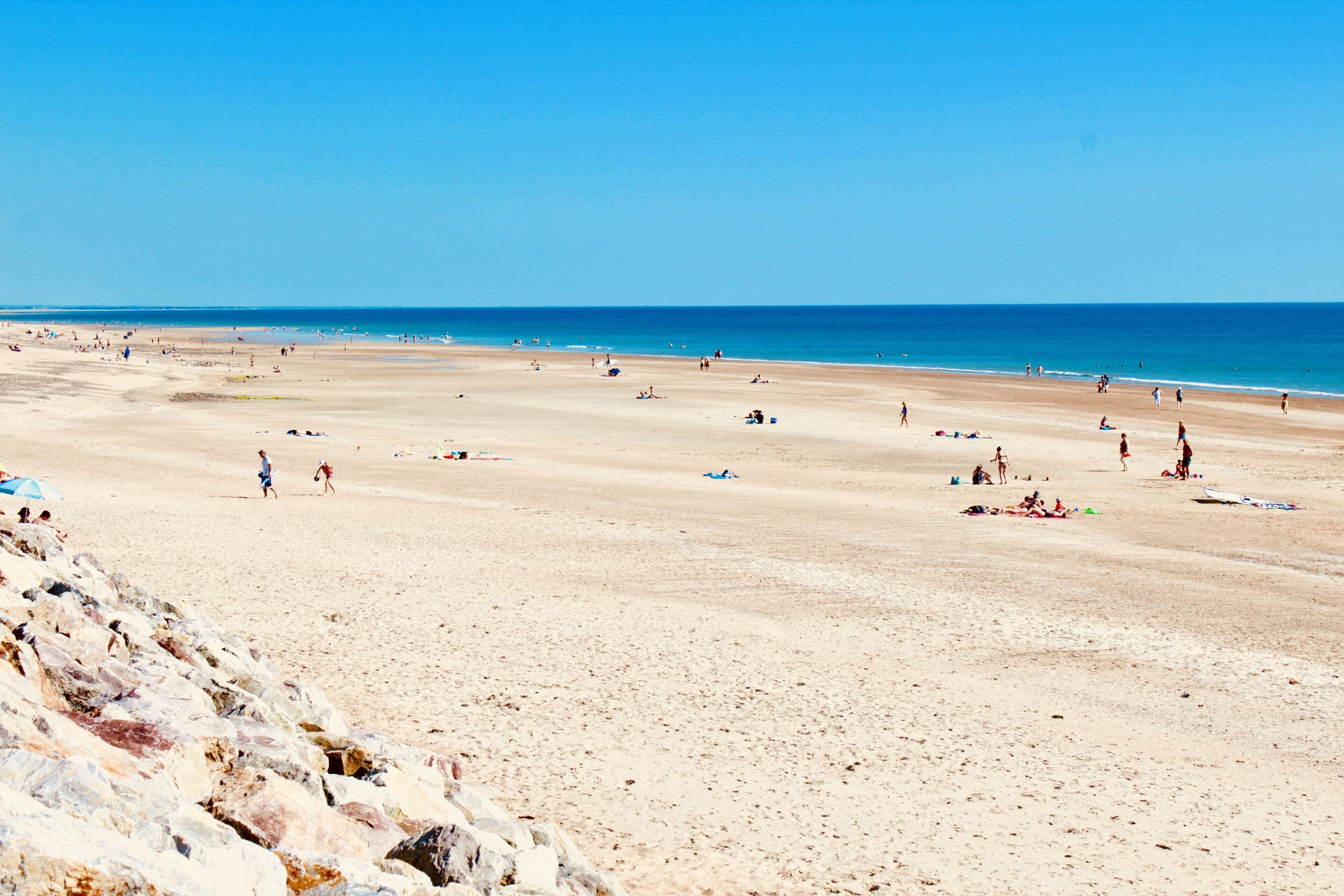 A wide sandy beach with people walking and relaxing.
