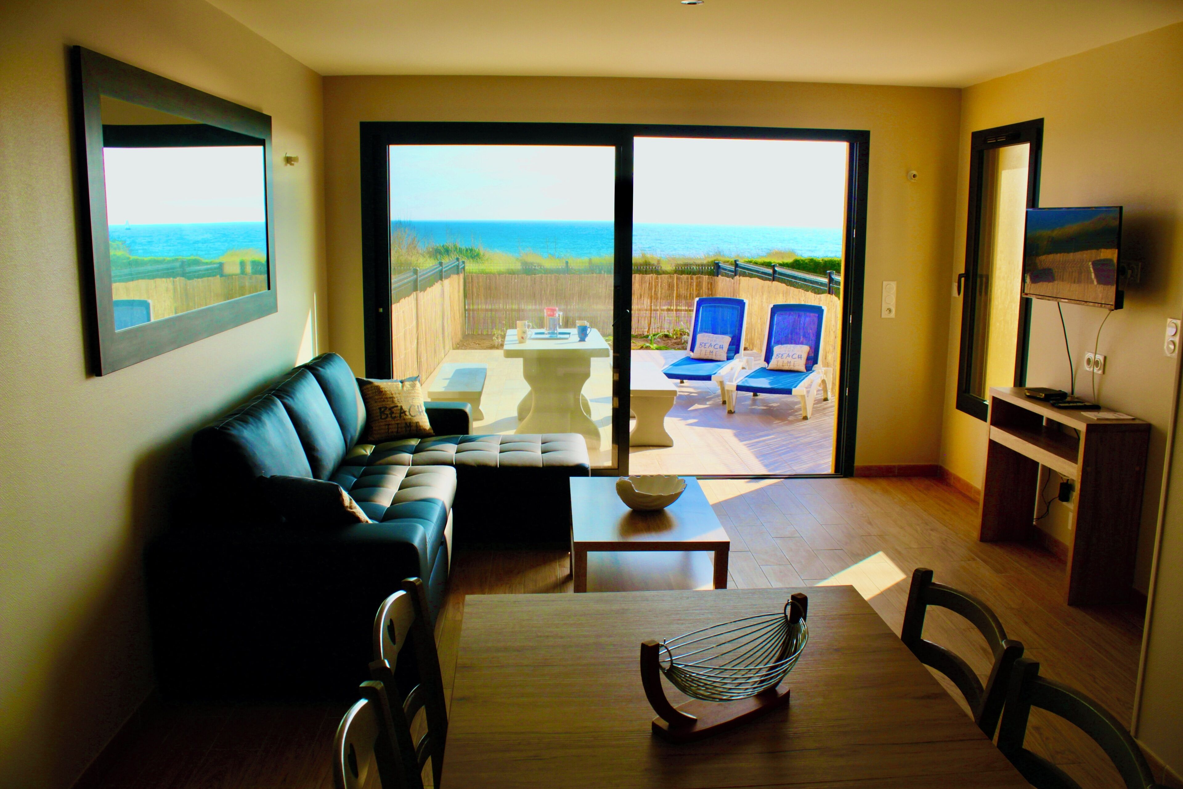 Una sala de estar con sofá, una mesa de comedor y vista a la playa a través de puertas corredizas de vidrio.