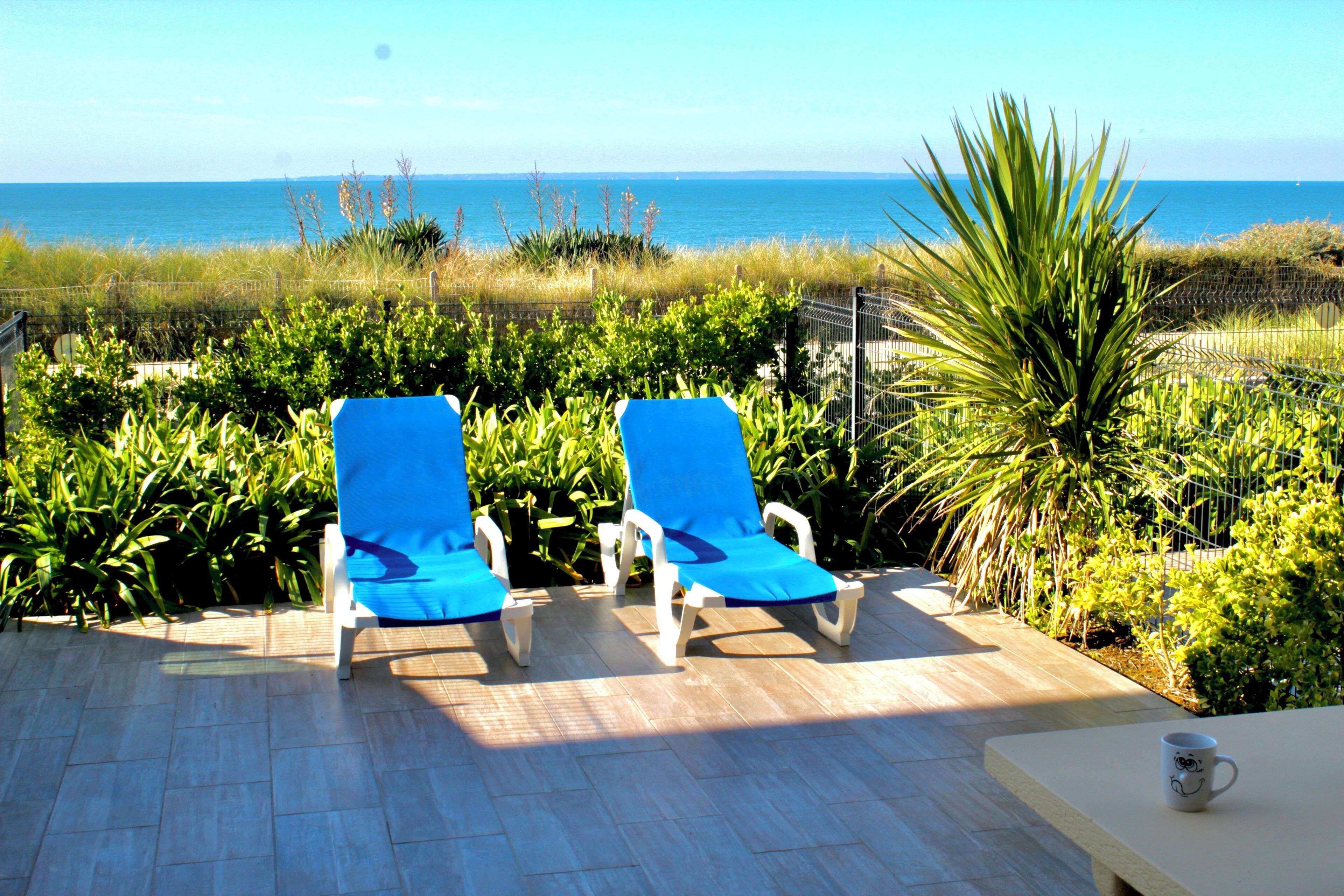 Two blue lounge chairs on a tiled patio with a view of the ocean.