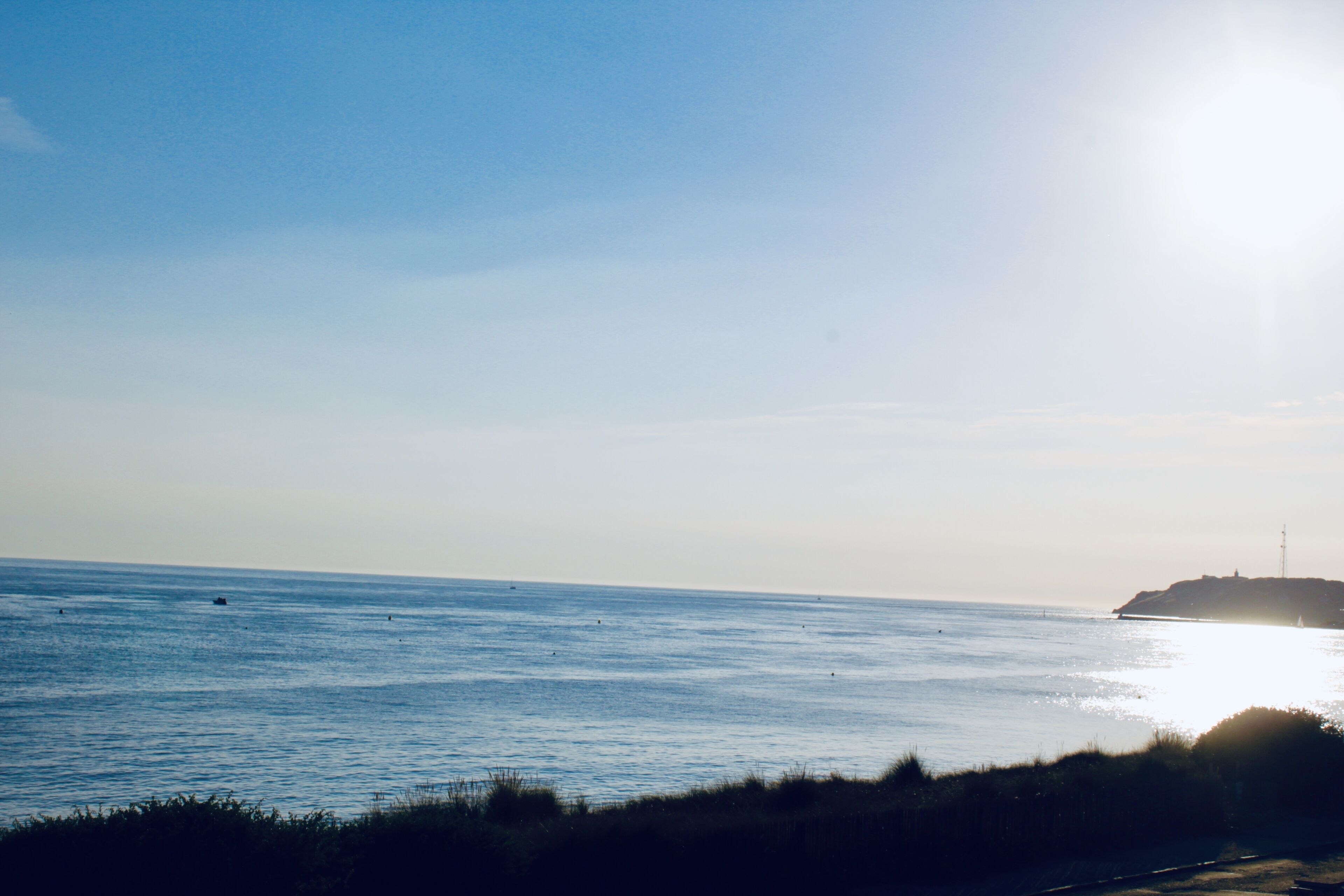 A coastal view with a lighthouse on a small island, calm sea, and clear sky.