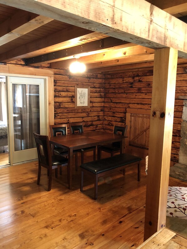 Un intérieur en bois avec une table et des chaises, un tableau encadré au mur et une porte dotée d’un panneau en verre.