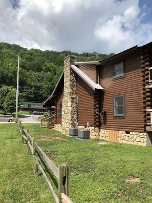 Une cabane en rondins avec une cheminée en pierre, une véranda et une vue sur une colline boisée.