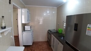 Una cucina compatta con mobili bianchi, un forno a microonde, un piccolo frigorifero e un frigorifero in acciaio inossidabile.