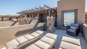 Een terras met lounge fauteuils en een rieten stoel, stenen pilaren en een pergola.