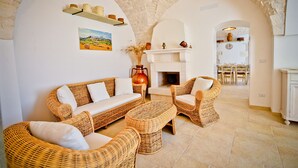 Una habitación acogedora con un arco de piedra, chimenea, muebles de mimbre y un área de comedor al fondo.