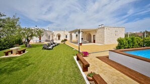 Una villa con piscina, césped cuidado y zonas de estar al aire libre.