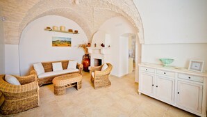 Una sala de estar acogedora con un arco de piedra, muebles de mimbre, una chimenea y un armario blanco.