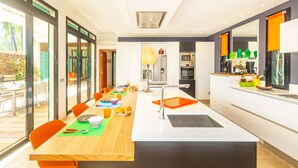 A modern kitchen with a central island, a dining area with orange chairs, and a view of the outdoors. - La Musarde, magnificent villa with swimming pool close to the beach of Boucan Canot (Boucan Canot)