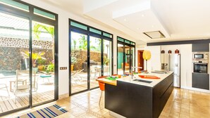 A modern kitchen with a large island, sliding glass doors to a patio, and a stone wall. - La Musarde, magnificent villa with swimming pool close to the beach of Boucan Canot (Boucan Canot)