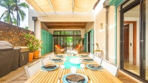 An outdoor dining area with a wooden table set for six, surrounded by chairs, with a stone wall and potted plants in the background. - La Musarde, magnificent villa with swimming pool close to the beach of Boucan Canot (Boucan Canot)