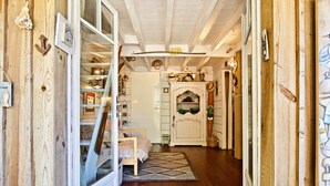 A narrow hallway with wooden walls, a bed with a white headboard, a small table, and a cabinet with decorative items. - Second line: pretty hut in the 44 Hectares (Lège-Cap-Ferret)