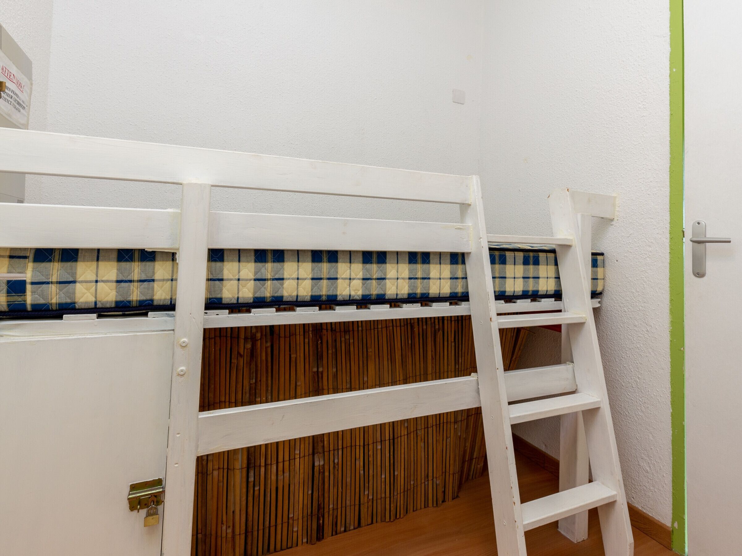 Een stapelbed met een geruit matras en een ladder.