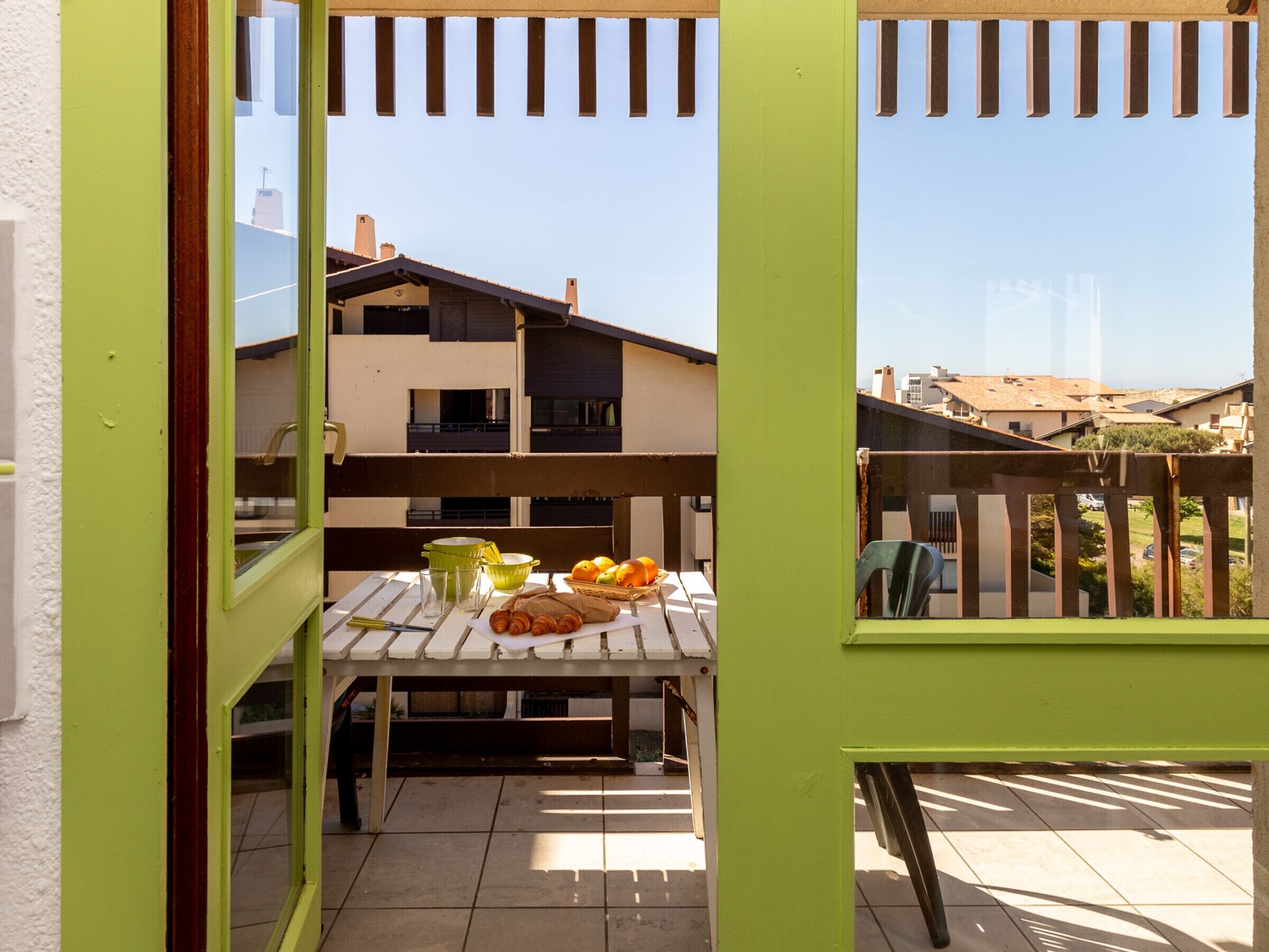 A balcony with a table set for breakfast, a view of residential buildings, and a clear sky.