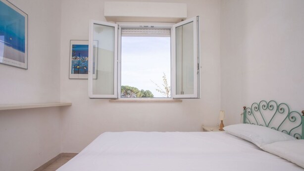 A bedroom with a bed, a window, a nightstand, and a wall-mounted shelf. - N110 - Numana, villa with garden and sea view (Numana)