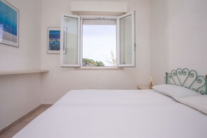 A bedroom with a bed, a window, a nightstand, and a wall-mounted shelf.